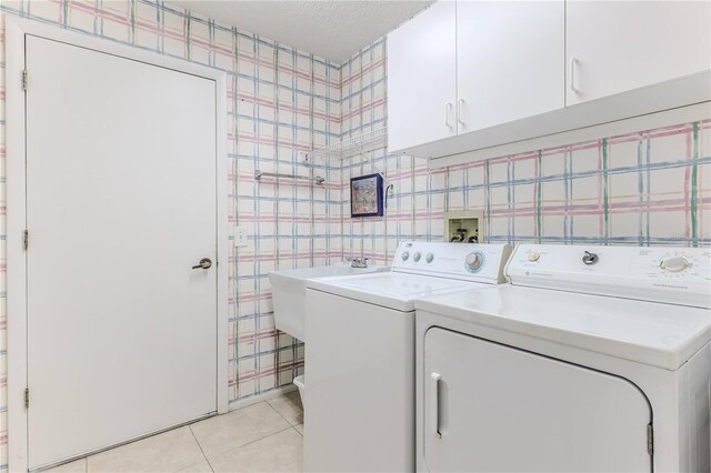 laundry room with wallpapered walls, washing machine and clothes dryer, cabinet space, light tile patterned flooring, and a textured ceiling