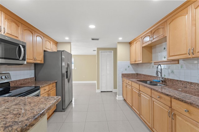 kitchen with appliances with stainless steel finishes, a sink, baseboards, dark stone countertops, and decorative backsplash