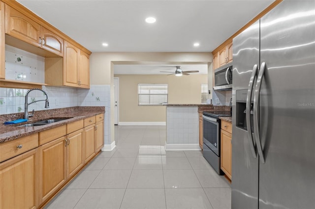 kitchen with stainless steel appliances, a sink, baseboards, dark stone countertops, and backsplash