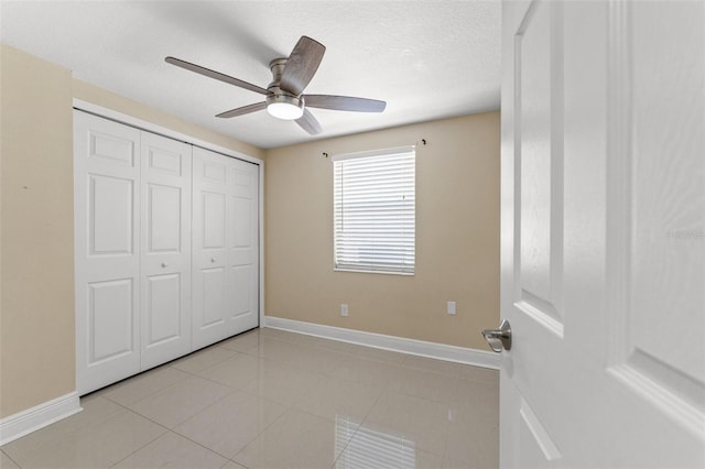 unfurnished bedroom with baseboards, light tile patterned floors, a closet, a ceiling fan, and a textured ceiling