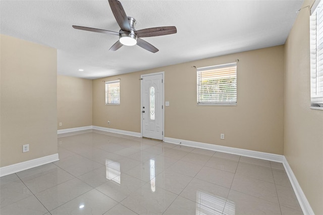 spare room featuring light tile patterned floors, healthy amount of natural light, a ceiling fan, and baseboards