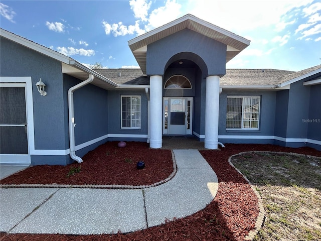 doorway to property featuring a shingled roof and stucco siding