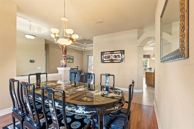 dining room featuring plenty of natural light, baseboards, arched walkways, wood finished floors, and crown molding