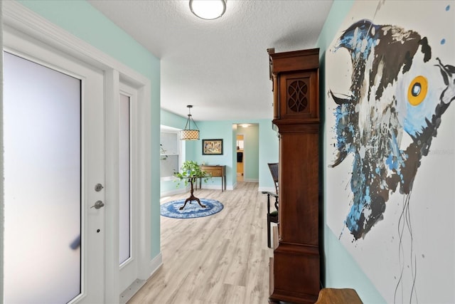 hallway featuring light wood-type flooring, a textured ceiling, and baseboards