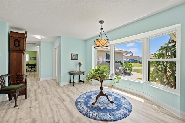 dining area featuring light wood-style floors, baseboards, healthy amount of natural light, and a textured ceiling