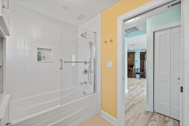 full bathroom featuring wood finished floors, combined bath / shower with glass door, baseboards, and a textured ceiling