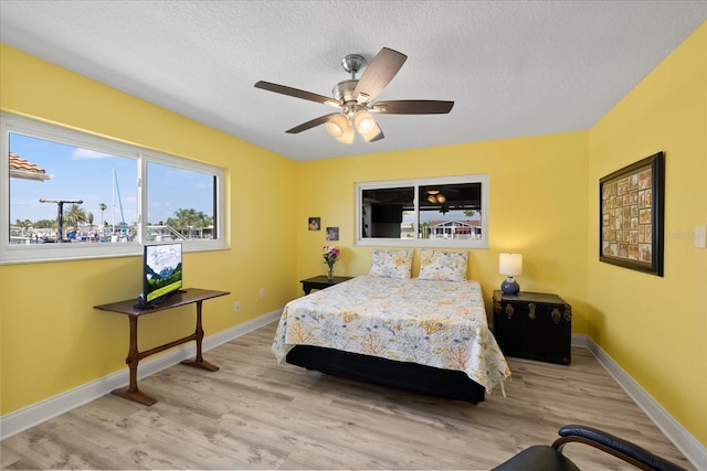 bedroom featuring wood finished floors, baseboards, a textured ceiling, and a ceiling fan
