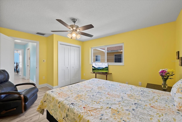 bedroom with light wood-type flooring, a closet, baseboards, a ceiling fan, and a textured ceiling