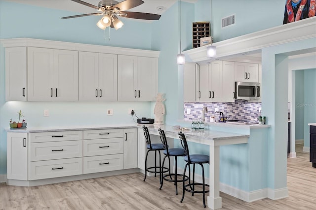 kitchen featuring stainless steel microwave, white cabinetry, backsplash, a ceiling fan, and a high ceiling