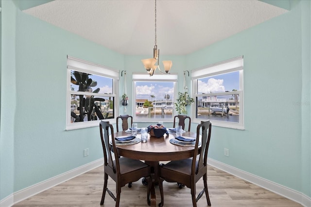 dining area with a chandelier, light wood-style floors, baseboards, and a textured ceiling