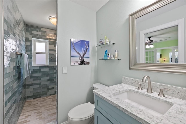bathroom with toilet, a tile shower, vanity, and ceiling fan