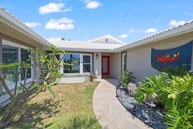 entrance to property featuring stucco siding, a tiled roof, and a yard