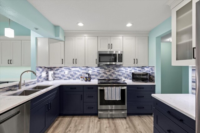 kitchen with appliances with stainless steel finishes, a sink, white cabinets, tasteful backsplash, and light wood-style flooring