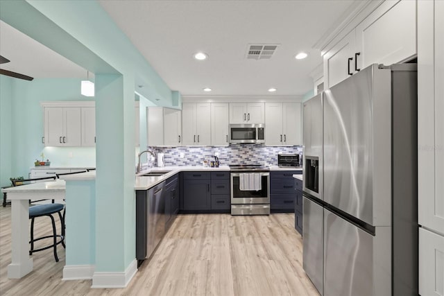 kitchen featuring stainless steel appliances, a sink, light wood-style floors, white cabinetry, and backsplash