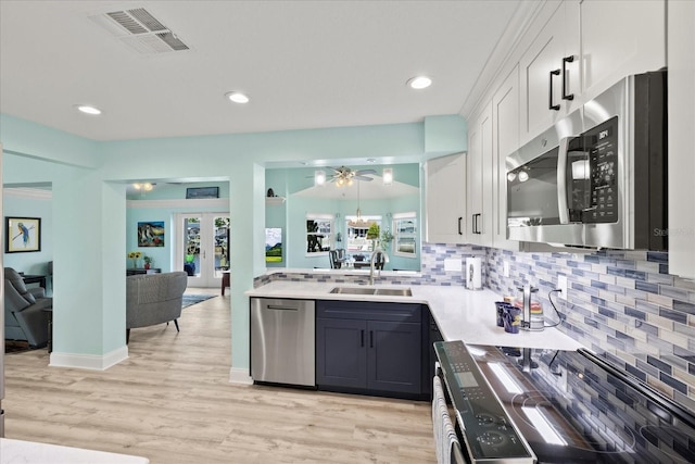 kitchen featuring appliances with stainless steel finishes, a sink, backsplash, white cabinets, and plenty of natural light