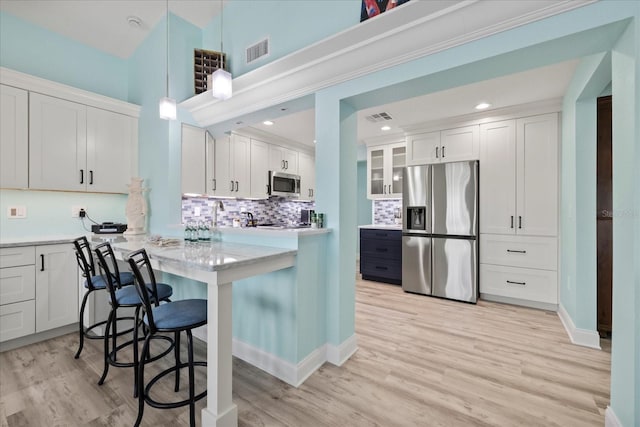 kitchen featuring appliances with stainless steel finishes, a kitchen bar, white cabinets, backsplash, and recessed lighting