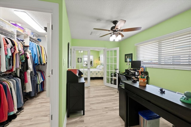 bedroom with french doors, multiple windows, light wood-type flooring, a textured ceiling, and a walk in closet
