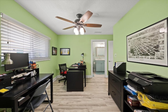 office featuring light wood-type flooring, a ceiling fan, a textured ceiling, baseboards, and a sink