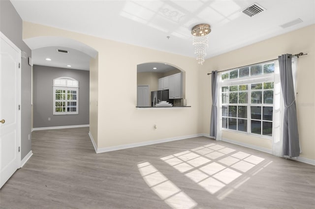 empty room featuring light wood finished floors, baseboards, recessed lighting, and arched walkways