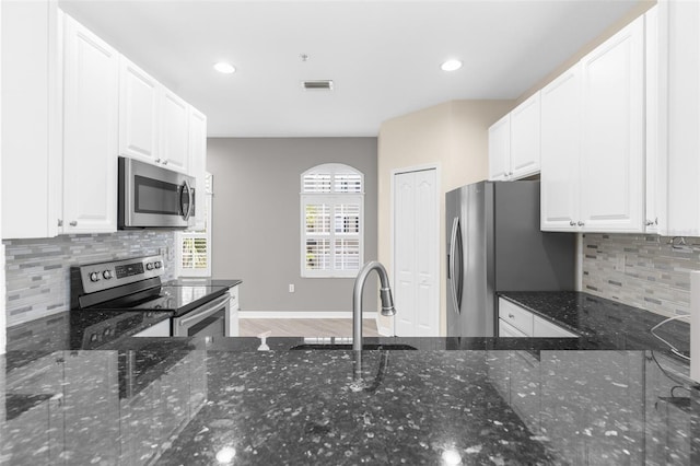 kitchen featuring stainless steel appliances, a sink, backsplash, dark stone counters, and recessed lighting