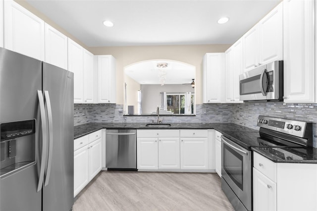 kitchen featuring stainless steel appliances, a sink, arched walkways, light wood finished floors, and decorative backsplash