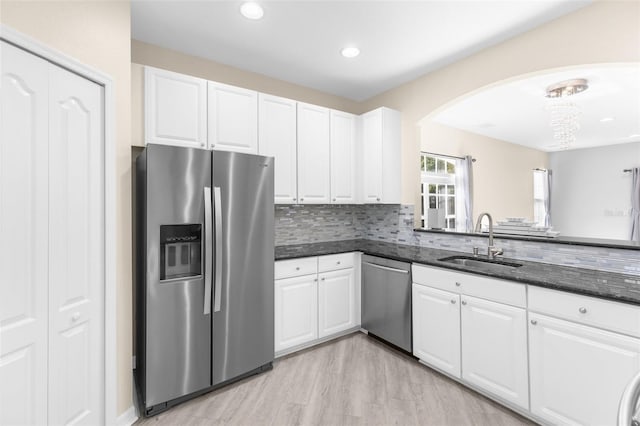 kitchen with stainless steel appliances, a sink, arched walkways, white cabinets, and dark stone counters