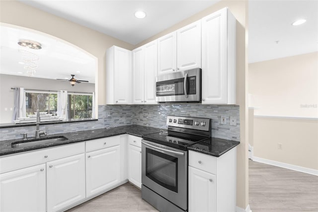 kitchen with appliances with stainless steel finishes, a sink, dark stone counters, decorative backsplash, and white cabinets