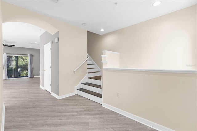 hallway with arched walkways, recessed lighting, wood finished floors, baseboards, and stairway