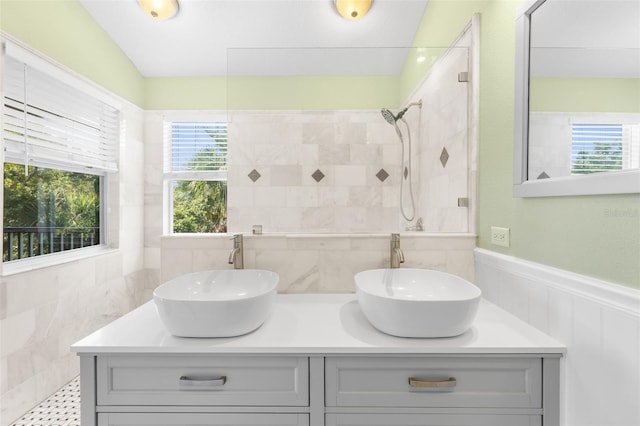 full bathroom featuring wainscoting, a tile shower, and double vanity