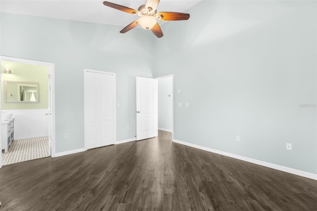 unfurnished bedroom featuring high vaulted ceiling, dark wood-style flooring, connected bathroom, baseboards, and a closet