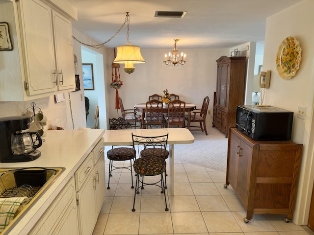kitchen featuring black microwave, a chandelier, light countertops, backsplash, and hanging light fixtures
