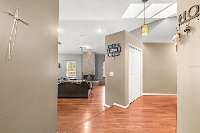 hall with a skylight, wood finished floors, baseboards, and lofted ceiling