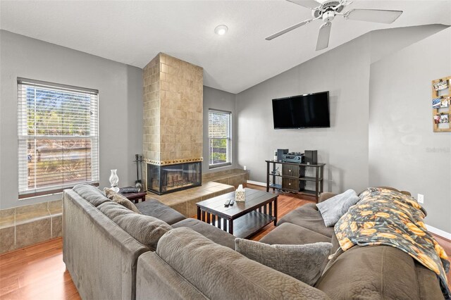living area with light wood-type flooring, lofted ceiling, a fireplace, and a ceiling fan