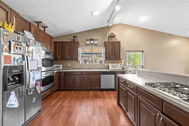 kitchen featuring stainless steel appliances, lofted ceiling, light countertops, wood finished floors, and a sink