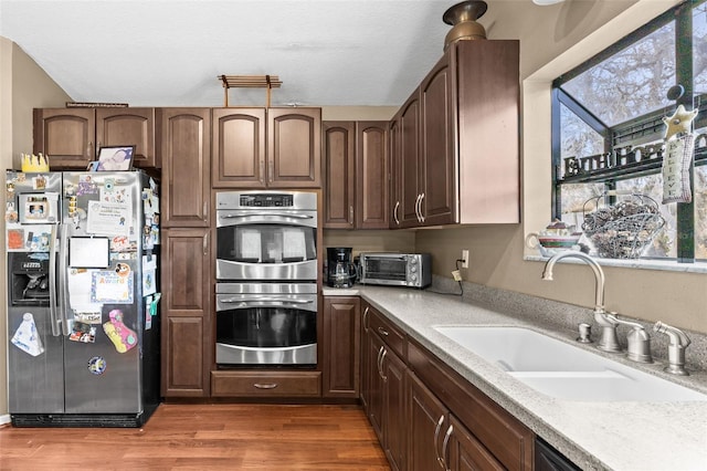 kitchen featuring stainless steel appliances, a sink, wood finished floors, light countertops, and a textured ceiling