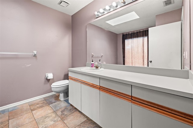 bathroom with baseboards, toilet, vanity, stone finish floors, and a skylight