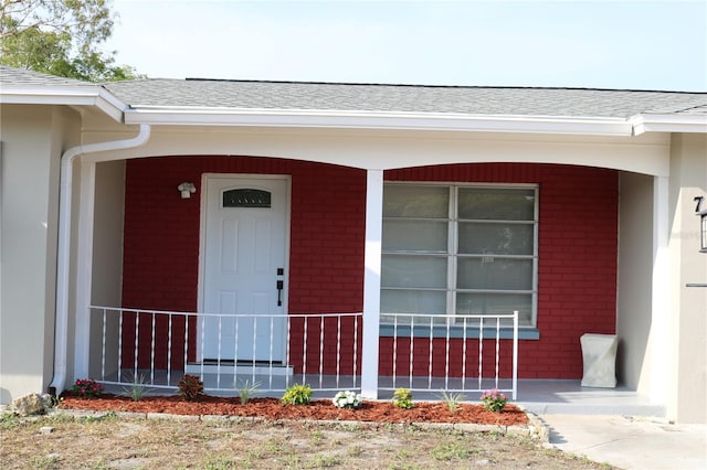 property entrance featuring brick siding, roof with shingles, and covered porch