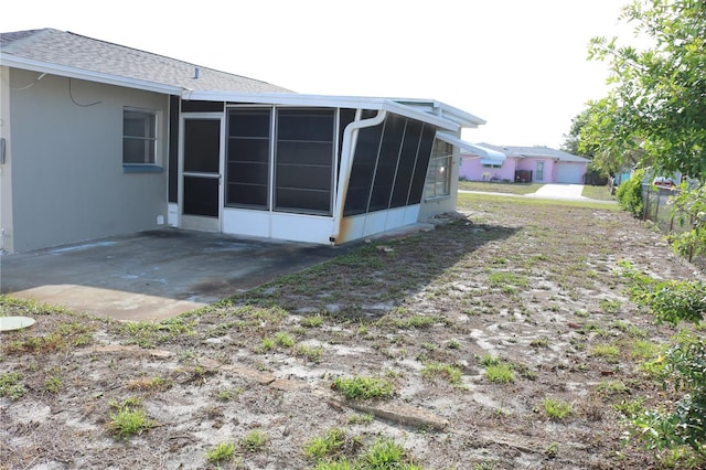 rear view of house featuring a sunroom, roof with shingles, and a patio area