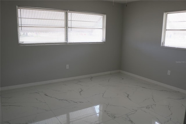 spare room with baseboards, marble finish floors, and plenty of natural light