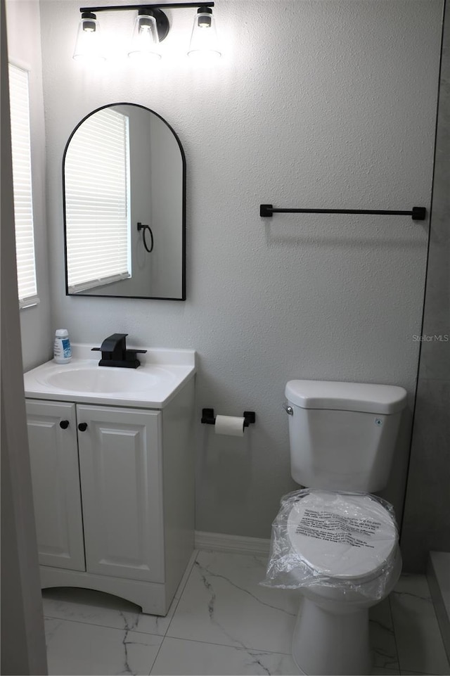 bathroom featuring marble finish flooring, toilet, vanity, and baseboards