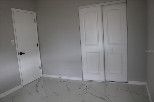 unfurnished bedroom with baseboards, marble look tile flooring, and a closet