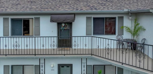 view of side of home with roof with shingles, stucco siding, and a balcony