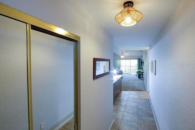 corridor with light tile patterned floors, light carpet, a textured ceiling, and baseboards