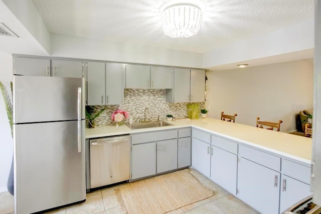 kitchen with appliances with stainless steel finishes, a sink, backsplash, light tile patterned flooring, and a chandelier
