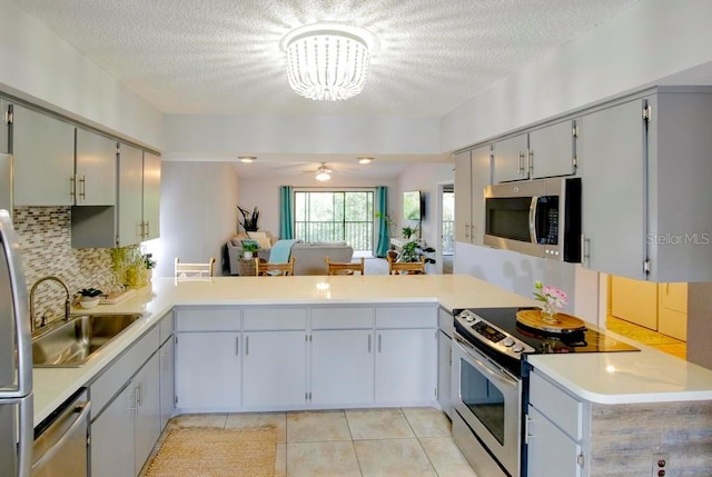 kitchen featuring appliances with stainless steel finishes, a sink, a chandelier, backsplash, and a textured ceiling