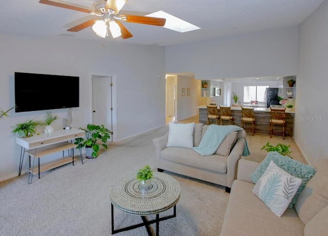 carpeted living room featuring a skylight, a ceiling fan, and baseboards