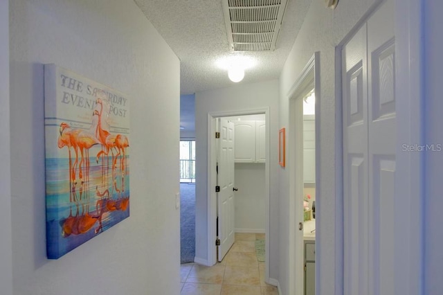 corridor featuring a textured ceiling, light tile patterned floors, and healthy amount of natural light