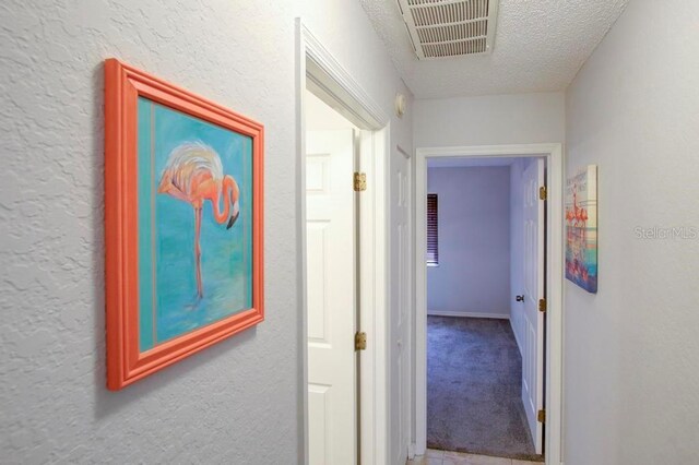 hall with a textured ceiling, a textured wall, and carpet flooring