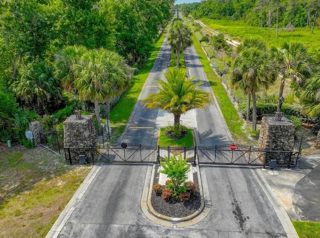 view of asphalt street featuring a gate, a gated entry, traffic signs, and curbs