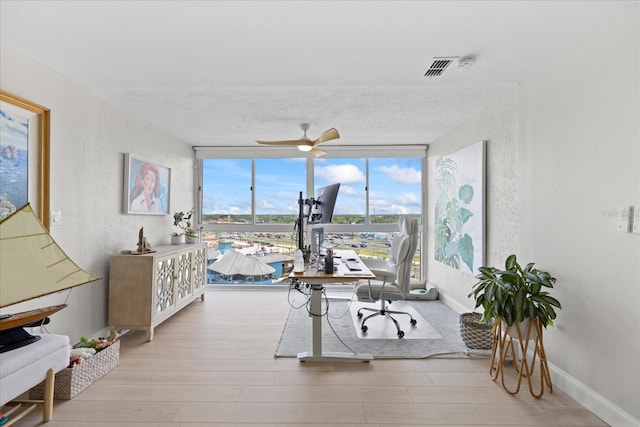 office space featuring wood finished floors, ceiling fan, expansive windows, baseboards, and a textured wall